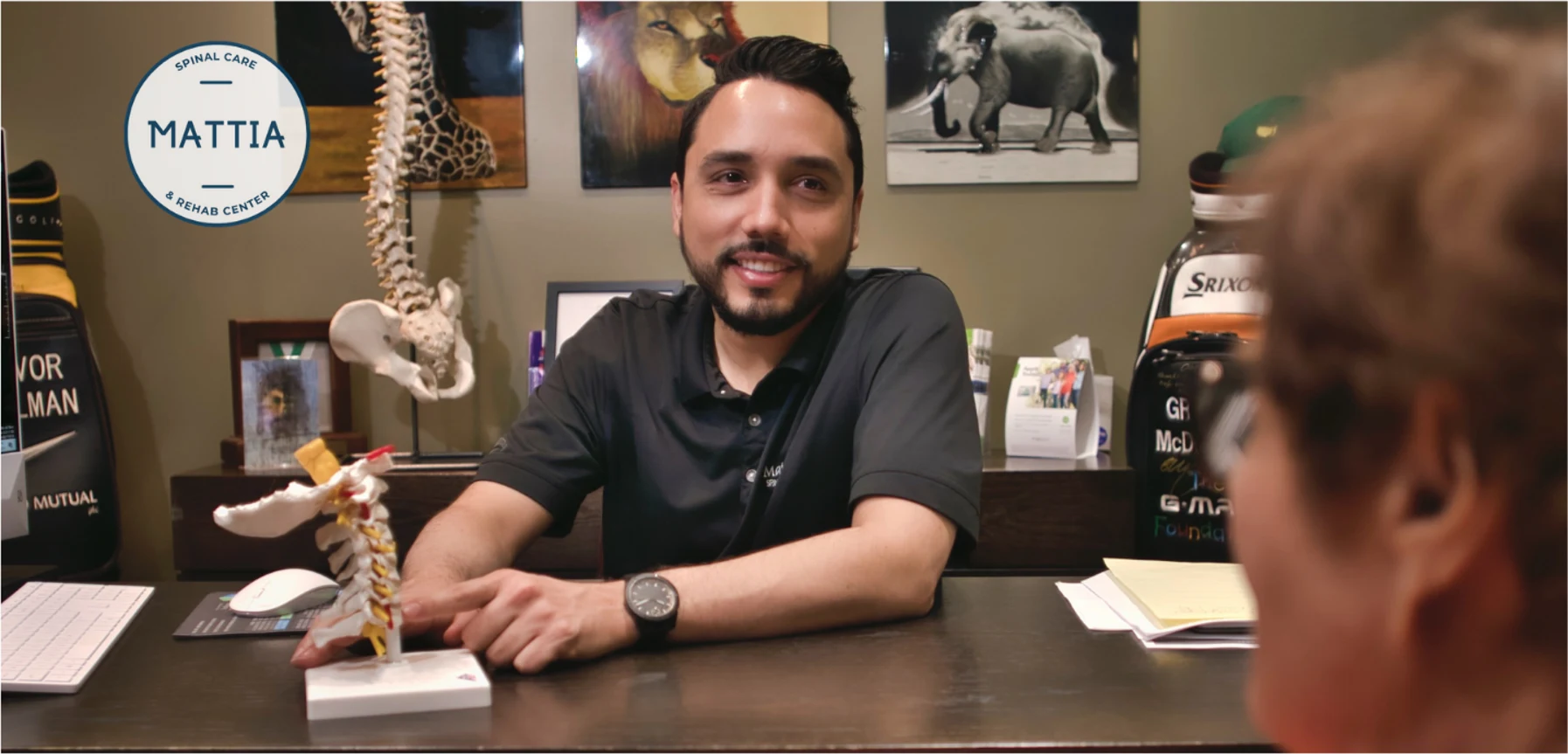 Orlando chiropractor Dr. Mattia consulting with a patient at the front desk, holding a cervical spine model